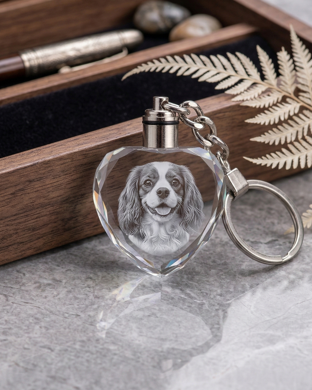 Heart-shaped keychain with engraved dog portrait in front of a wooden box.