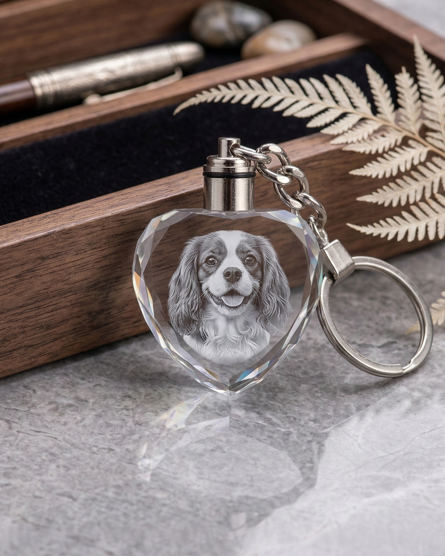 Heart-shaped keychain with engraved dog portrait in front of a wooden box.